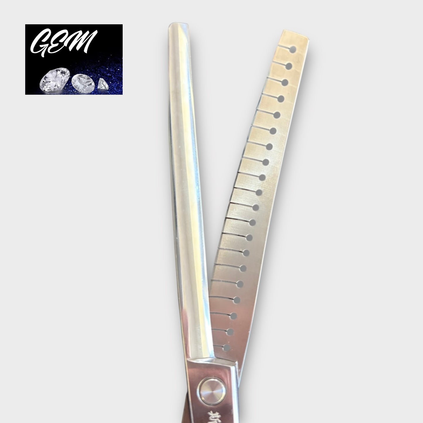 A close-up of the GEM Supreme Curved Chunkers 7.5" Scissors, crafted from Aichi steel—one blade is straight, the other serrated with holes. The top left displays the GEM logo above three gemstones on a dark blue background.