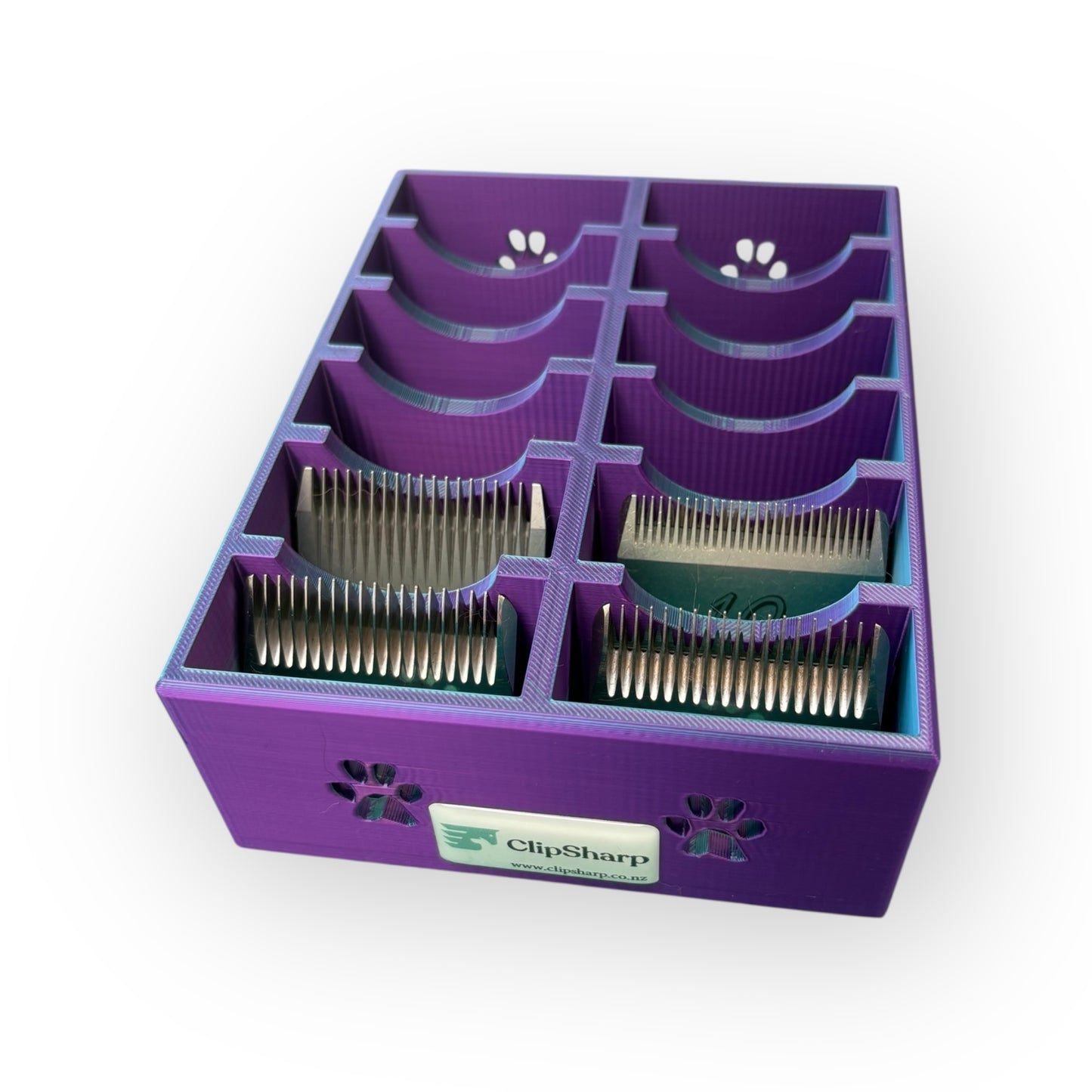 The Clip Sharp Standard Blade Tray is a purple plastic organizer with multiple slots for metal clipper blades, featuring small paw print cutouts and a "ClipSharp" label.