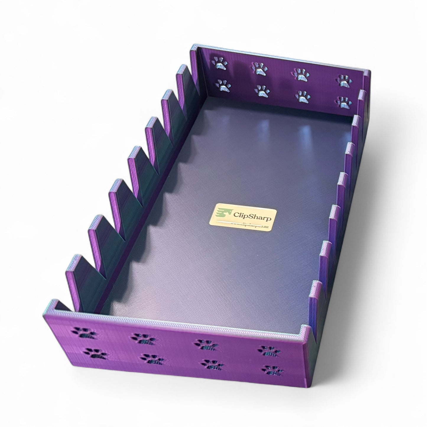 The Clip Sharp Scissor Tray is a rectangular, purple 3D printed organizer with vertical dividers and paw print cutouts. Its dark base features a “ClipSharp” sticker, and it's shown on a white background.