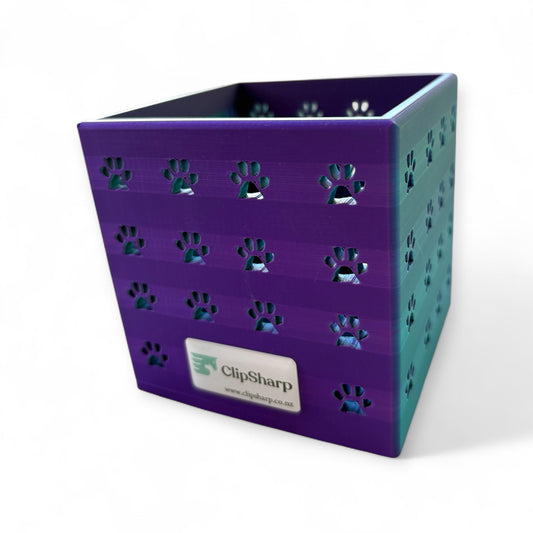 The Clip Sharp Small Storage Caddy is a purple and teal 3D printed organizer with paw print cutouts and a front label, ideal for storing combs and brushes. Shown against a plain white background.