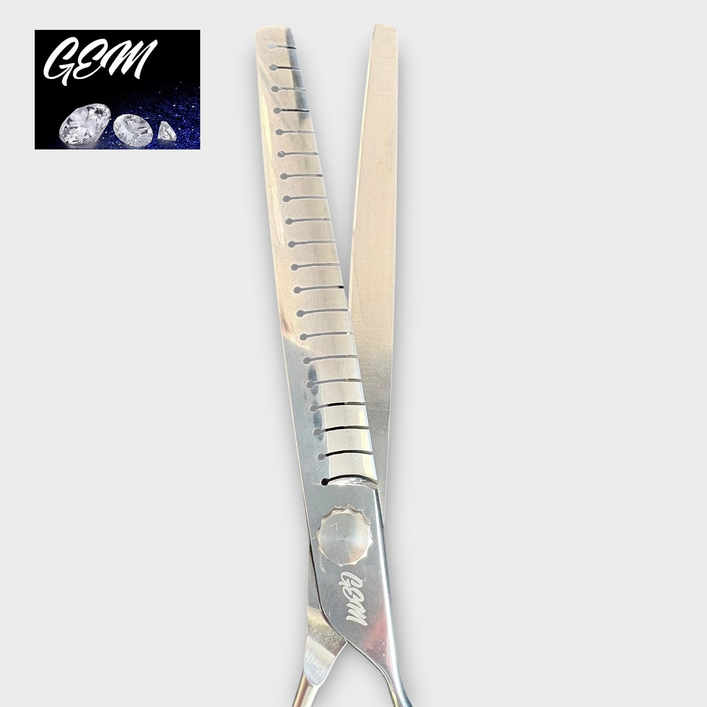 The GEM Supreme Straight Chunkers 7.5" scissors are made from Aichi steel with one serrated and one straight blade. "GEM" is engraved on the handle, and a GEM logo with three gemstones features in the top left corner.