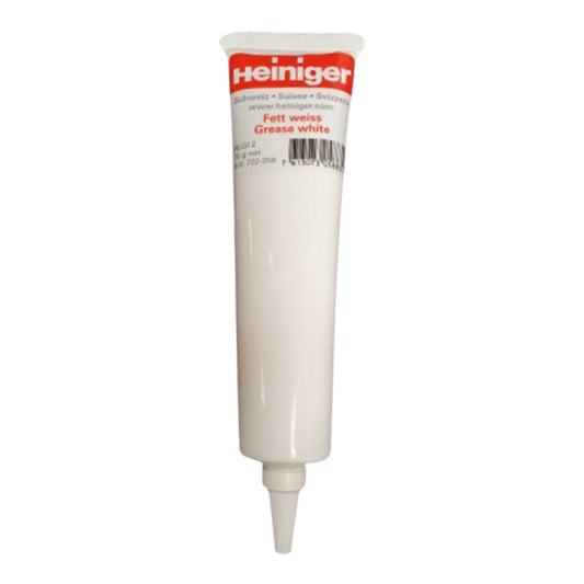 A white tube of Heiniger White Grease with a red and white cap, used for lubrication, is shown standing upright on a white background.