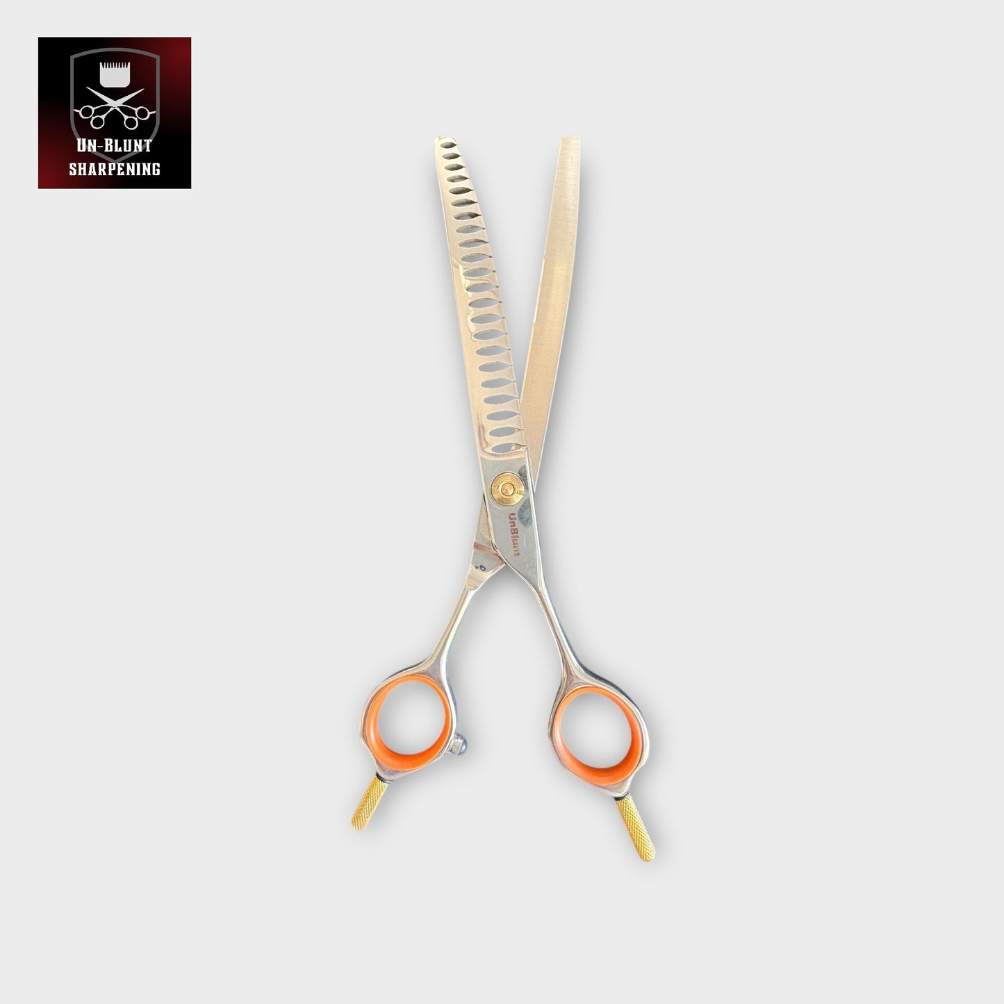 The UnBlunt Curved Chunkers 7" Scissors, featuring orange finger rings and gold accents, are shown open on a light background. The top left displays the UN-BLUNT SHARPENING logo with scissors and a crown.