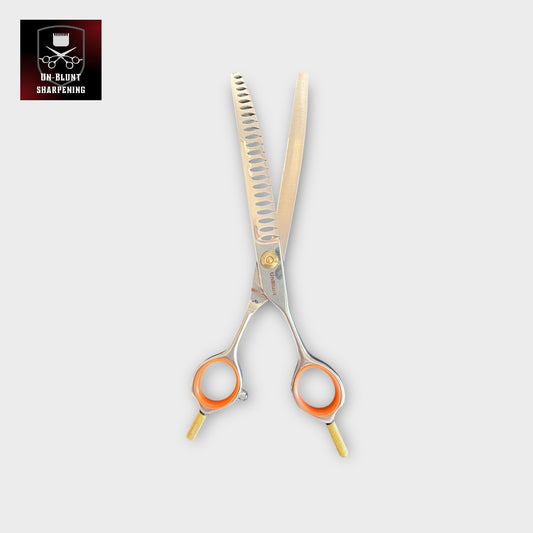The UnBlunt Curved Chunkers 7" Scissors, featuring orange finger rings and gold accents, are shown open on a light background. The top left displays the UN-BLUNT SHARPENING logo with scissors and a crown.