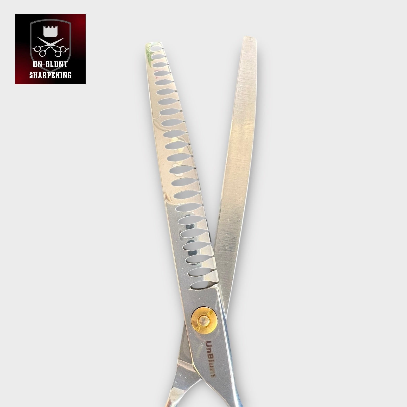 A pair of UnBlunt Curved Chunkers 7" scissors with serrated blades and a gold screw; the top left corner displays a logo showing a razor, comb, and scissors above the text "UN-BLUNT SHARPENING.