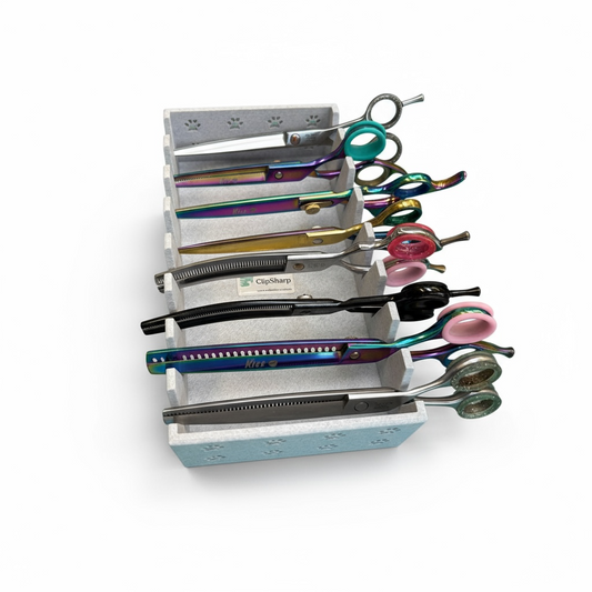 The Clip Sharp Scissor Tray, a white paw-print decorated 3D printed organizer, holds five pairs of colorful grooming scissors and shears in individual slots, neatly arranged on a white background.