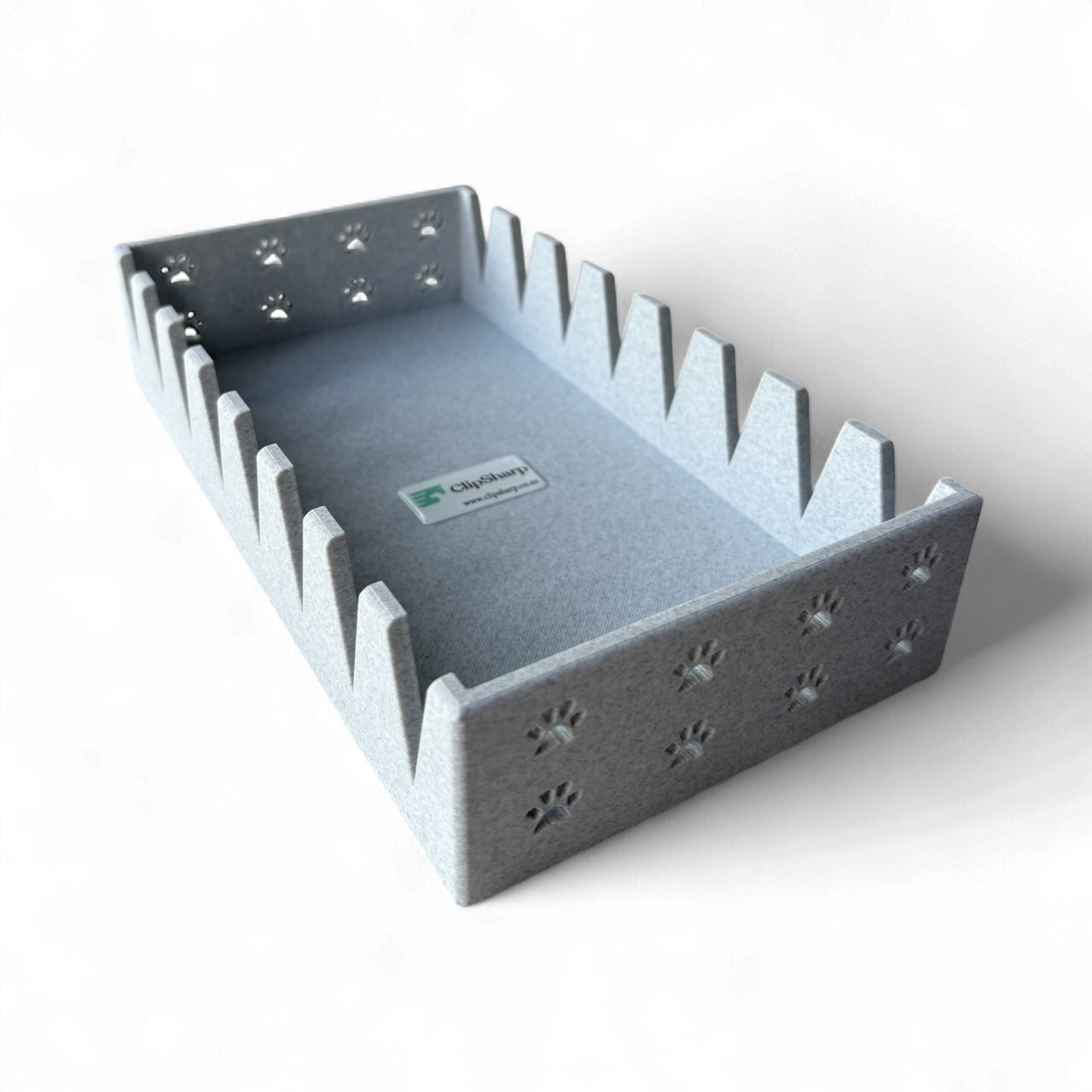 The Clip Sharp Scissor Tray is a rectangular gray felt organizer with tall zigzag sides and paw print cutouts on the short edges. Inside, a label with a green logo adds style to this secure storage solution for your scissors.